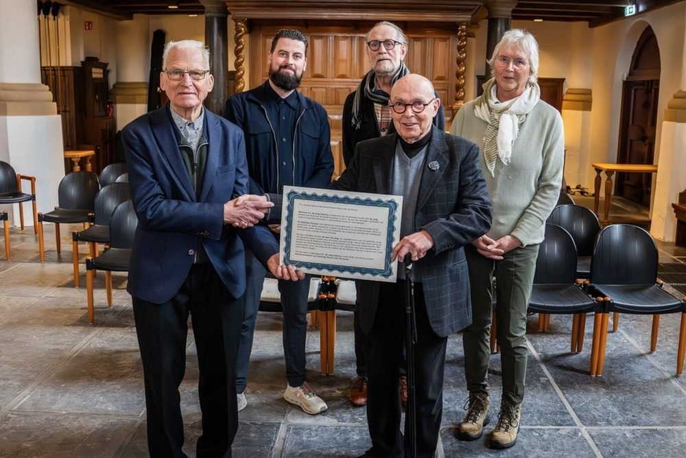 Vijf mensen in de Hobbe van Baerdtkerk. De heer A. S. de Jong houdt samen met bestuursleden van de stichting de oorkonde vast.